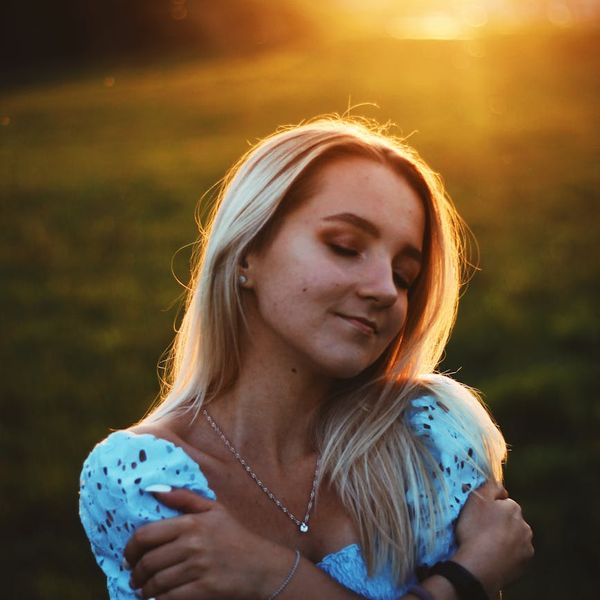 Person smiling and stretching gently outdoors with a serene natural background.